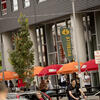 Angled photo of Potbelly restaurant on campus. Orange and red umbrellas line the walkway, and students move between classes and sit down to each lunch.
