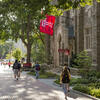 College students walk across campus on a sunny day with Temple University flag