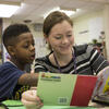 student teacher reading a book with an elementary school student.
